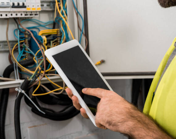 cropped image of electrician using tablet near electrical box in corridor